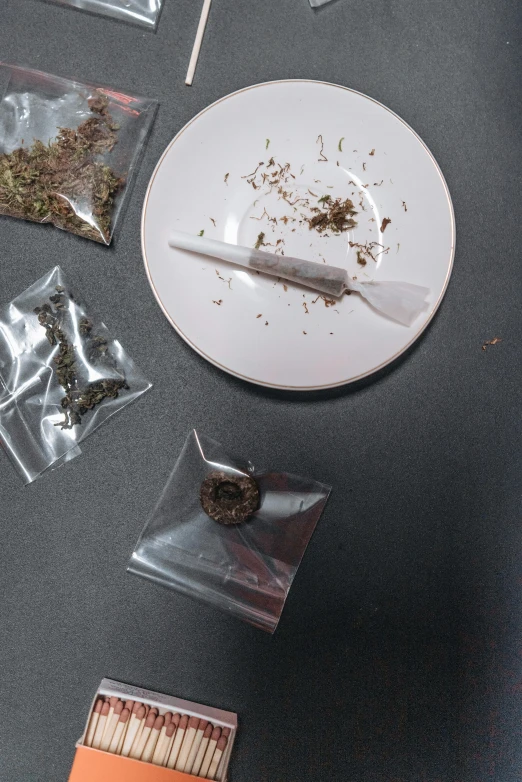 a white plate sitting on top of a table next to matches, pot leaf, seeds, in a lab, spoon placed