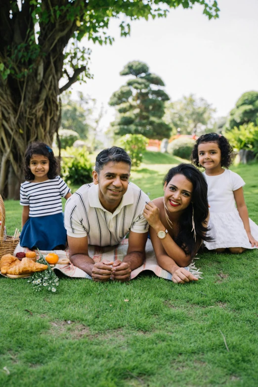 a group of people sitting on top of a lush green field, husband wife and son, having a picnic, press shot, jayison devadas