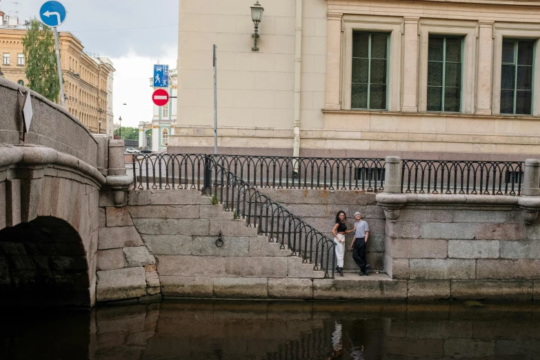 a couple sitting on a ledge next to a body of water, a picture, by Fyodor Rokotov, railing along the canal, walking down a marble stairwell, saint petersburg, museum photo