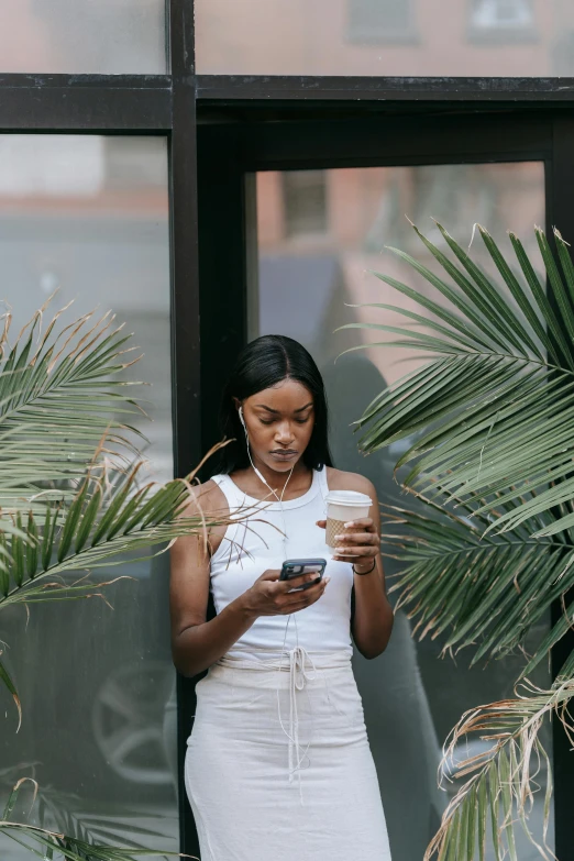 a woman in a white dress looking at her cell phone, by Cosmo Alexander, trending on unsplash, tall plants, dark skin tone, android coffee shop, palms