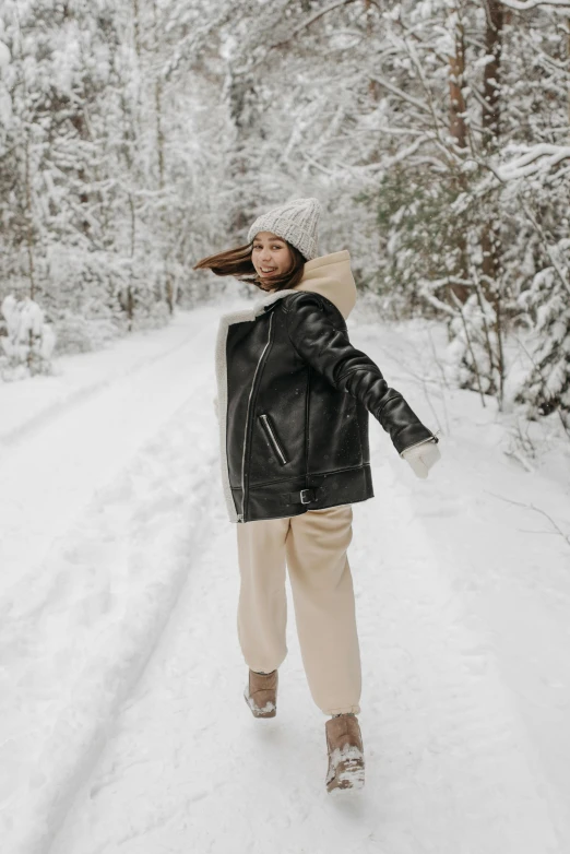 a woman walking down a snow covered road, by Julia Pishtar, trending on pexels, wearing a leather flight jacket, distorted pose, thumbnail, with black beanie on head