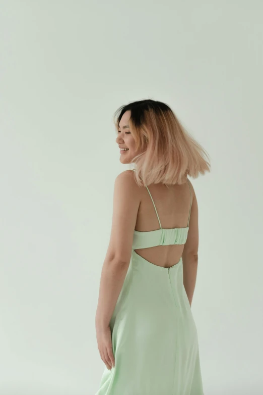 a woman standing in a light green dress, trending on pexels, back of the hair, heonhwa choe, on a pale background, kailee mandel