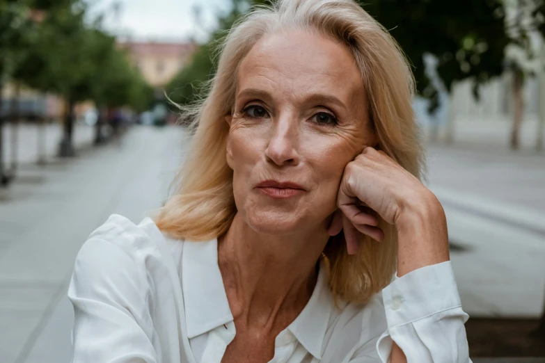 a woman in a white shirt sitting on a bench, a portrait, by Emma Andijewska, pexels contest winner, mature facial features, at a city street, avatar image, 5 5 yo