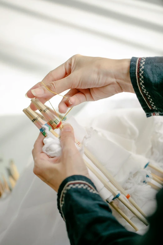 a close up of a person holding a pair of chopsticks, a cross stitch, by Ruth Jên, white and gold robes, vials, in a white boho style studio, creating a soft