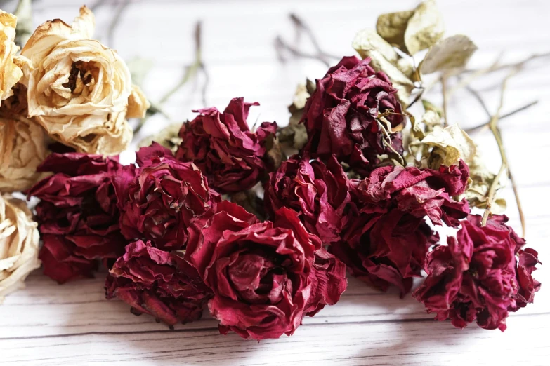a bunch of dried flowers sitting on top of a wooden table, inspired by Annie Rose Laing, unsplash, red roses, maroon, close up shot from the side, actors