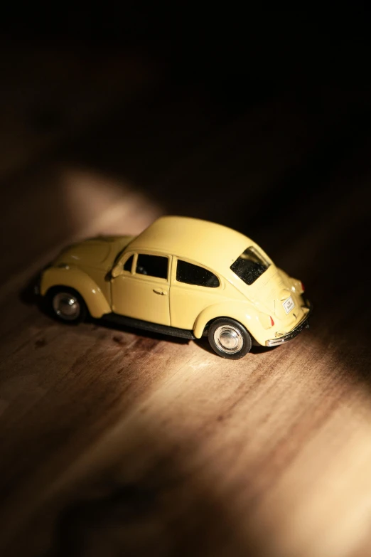 a toy car sitting on top of a wooden table, unsplash, photorealism, yellow artificial lighting, beetle, cream, high angle shot