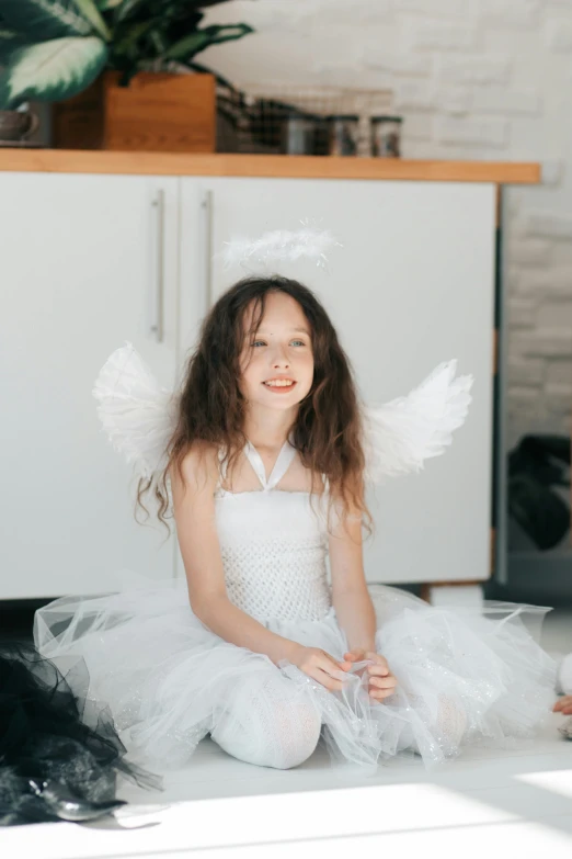 a little girl in a white dress sitting on the floor, inspired by Marie Angel, pexels contest winner, winged human, on kitchen table, holiday, 15081959 21121991 01012000 4k