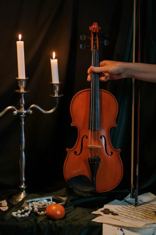 a violin sitting on top of a table next to a candle, standing on top of a violin, holding a bow, during the night