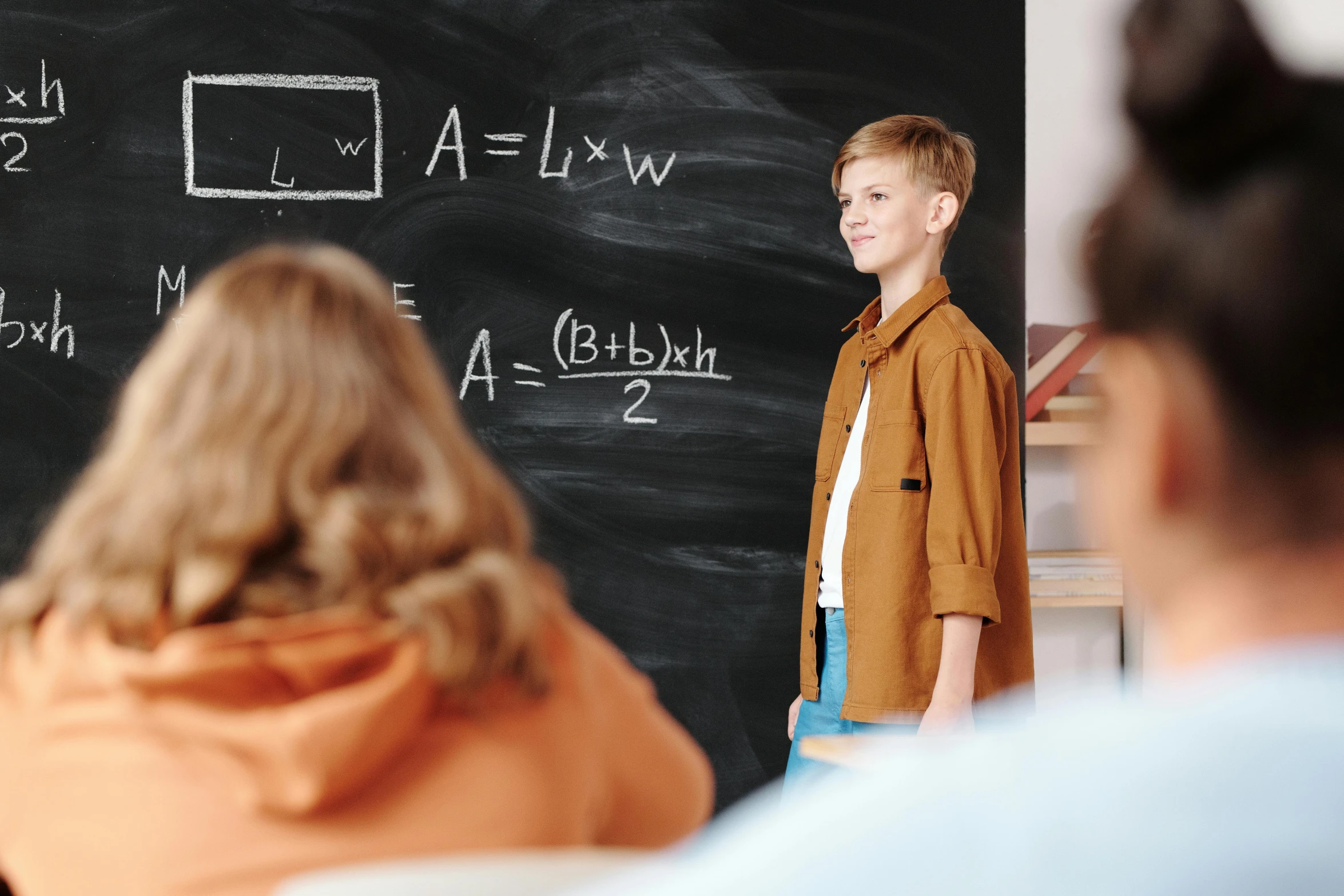 a boy standing in front of a blackboard in a classroom, by Adam Marczyński, pexels contest winner, audience in the background, pythagorean theorem, a person standing in front of a, lachlan bailey