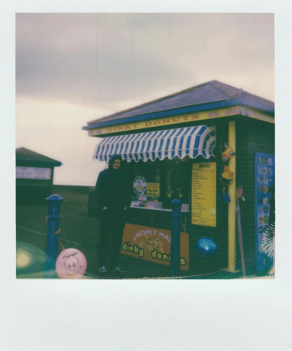 a man standing in front of a kiosk, a polaroid photo, by Nick Fudge, unsplash, private press, seaside, yellow awning, ice cream, scanned in
