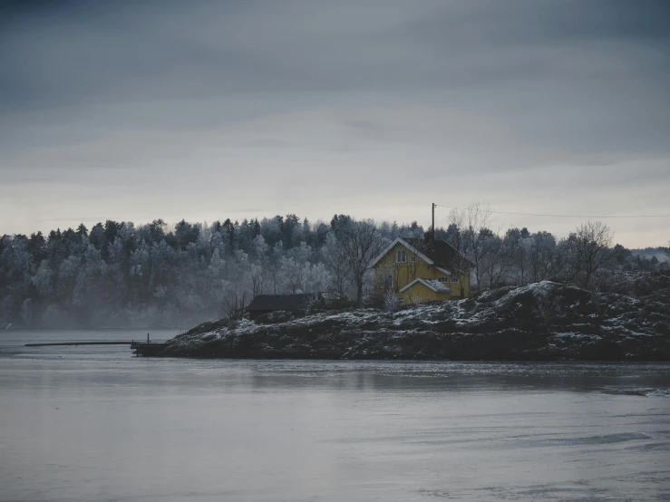 a yellow house sitting on top of a snow covered hill, inspired by Eero Järnefelt, pexels contest winner, tonalism, overcast lake, grey, an island, smoldering