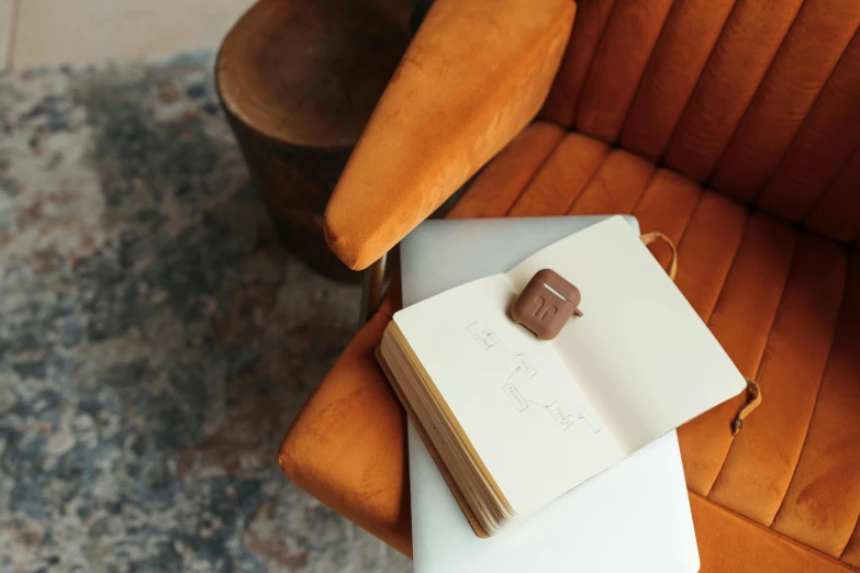 an open book sitting on top of a table next to a chair, trending on pexels, private press, chocolate, caramel, plush leather pad, found written in a notebook