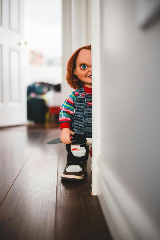 a doll sitting on top of a wooden floor, by Anson Maddocks, pexels, happening, holding a chainsaw, about to enter doorframe, chucky, walking towards camera