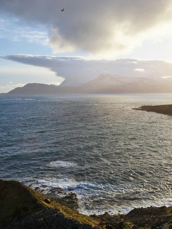 a bird flying over a body of water, inspired by Johan Christian Dahl, pexels contest winner, iceland hills in the background, stormy coast, today\'s featured photograph 4k, panorama distant view