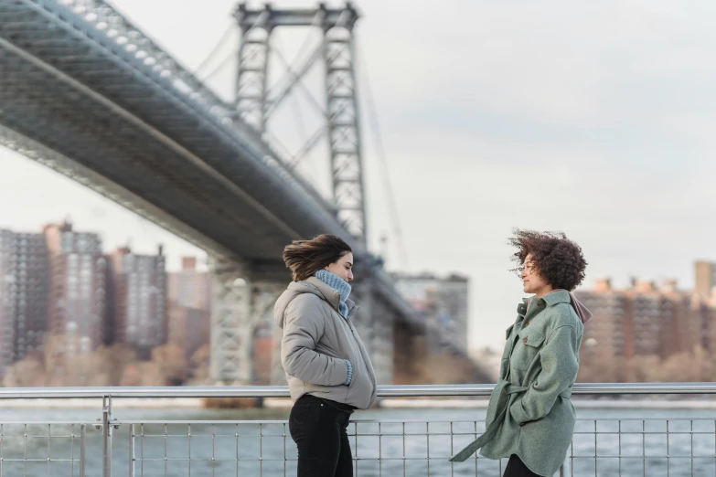 two women standing next to each other in front of a bridge, trending on unsplash, happening, new york backdrop, windy hair, rebecca sugar, ignant