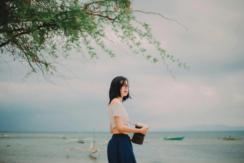 a woman standing on a beach next to the ocean, inspired by Itō Shinsui, pexels contest winner, dilraba dilmurat, medium format film photography, bali, avatar image