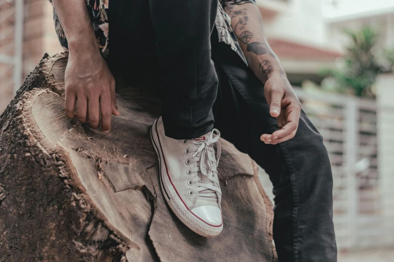 a man sitting on top of a tree stump, trending on pexels, hyperrealism, blue jeans and grey sneakers, gray skin. grunge, tattoos all over the skin, wearing white sneakers