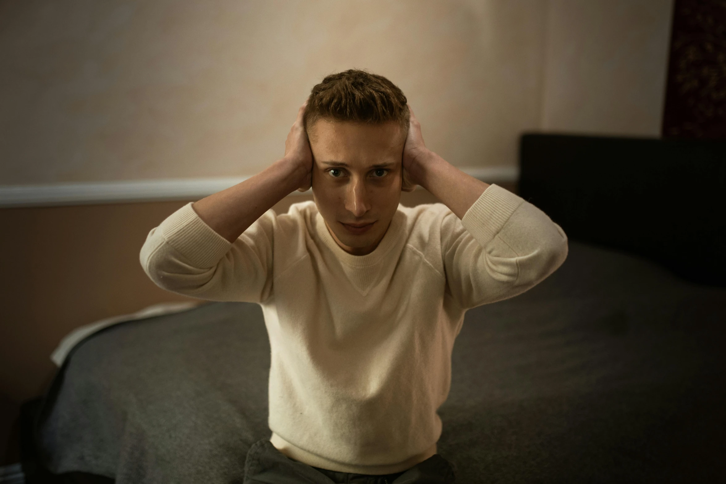 a man sitting on a bed with his hands on his head, unsplash, hyperrealism, ryan gosling, tinnitus, around 1 9 years old, medium portrait soft light