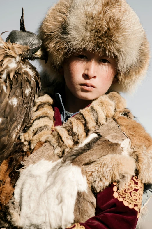 a man in a fur hat holding an owl, an album cover, inspired by Kanō Tan'yū, trending on pexels, mongolia, teen boy, russian costume, eagle feather