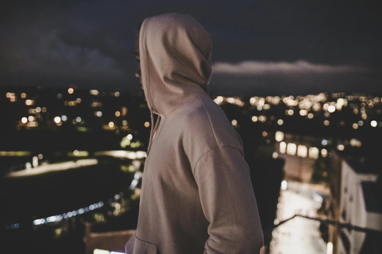 a man in a hoodie looking out over a city at night, trending on pexels, beige hoodie, background image, high angle close up shot, instagram picture