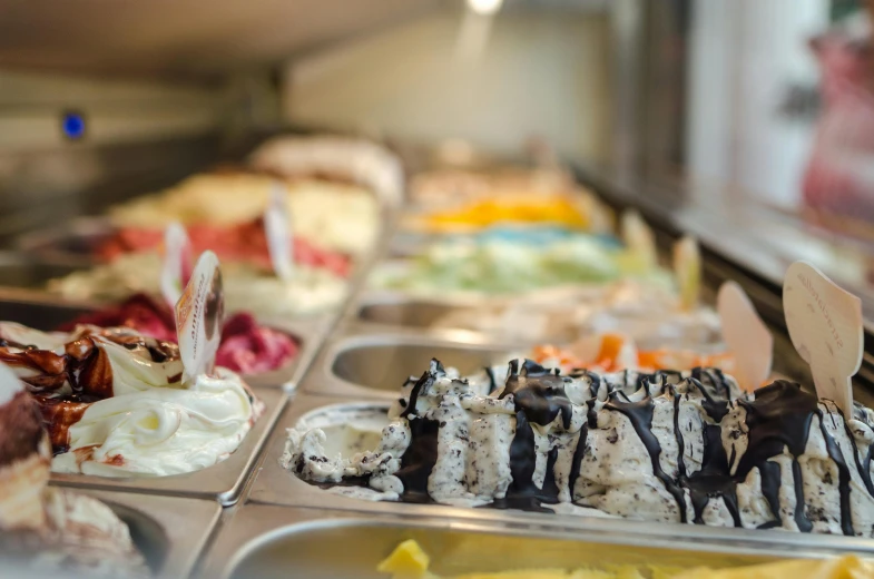 a display case filled with lots of different types of ice cream, by Matthias Stom, trending on unsplash, fan favorite, hands on counter, panoramic shot, sundown