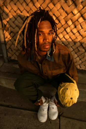a man with dreadlocks sitting on the ground, holding a ball, playboi carti portrait, promotional image, (golden hour)