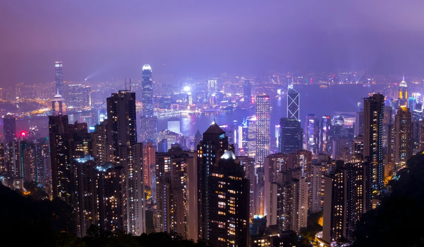 a view of a city at night from the top of a mountain, hong kong buildings, purple - tinted, foster and partners, multicoloured