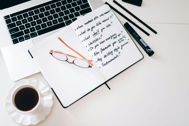 an open notebook sitting on top of a desk next to a cup of coffee, trending on unsplash, wearing black rimmed glasses, white background”, instagram post, background image