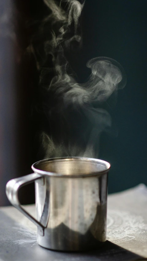 a steaming cup sitting on top of a table, by Dave Allsop, pexels, shiny silver, soft smoke, mint, indoor shot