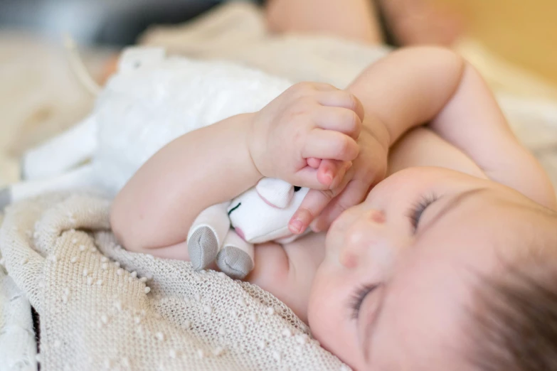a close up of a baby laying on a bed, by Arabella Rankin, pexels contest winner, happening, holding a rabbit, toy photo, eyes closed, product shot