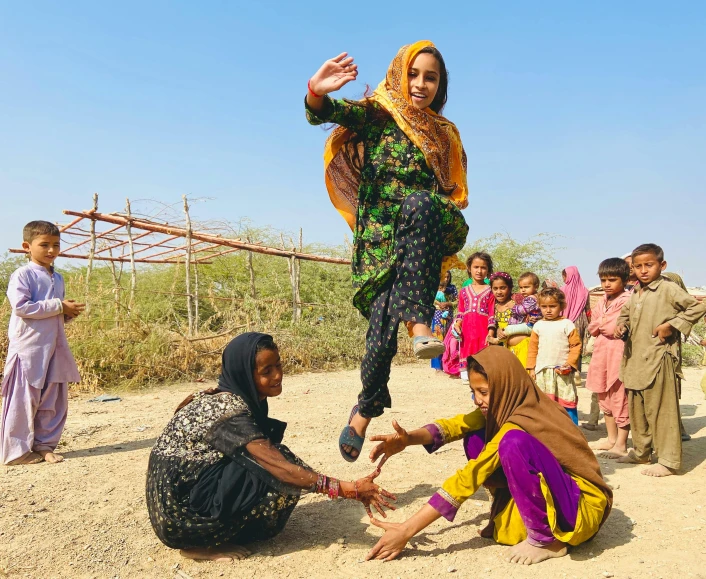 a group of people standing on top of a dirt field, by Arabella Rankin, pexels contest winner, arabesque, afghan girl, in a jumping float pose, on a village, standing on two legs