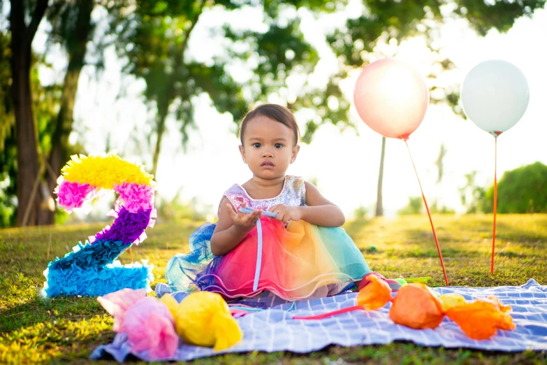 a baby girl sitting on a blanket with balloons, pexels contest winner, avatar image, multicoloured, picnic, cindy avelino