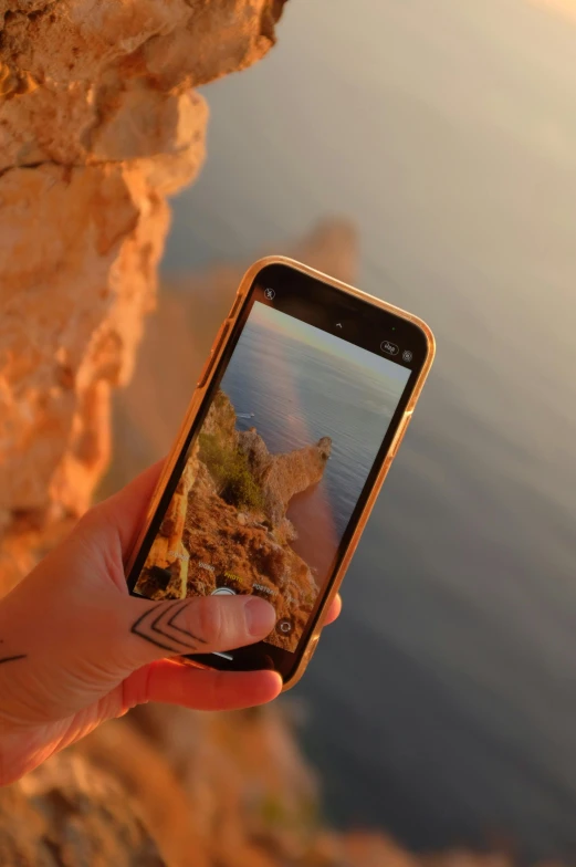 a person taking a picture with a cell phone, on a cliff, liquid gold, slightly pixelated, back facing the camera