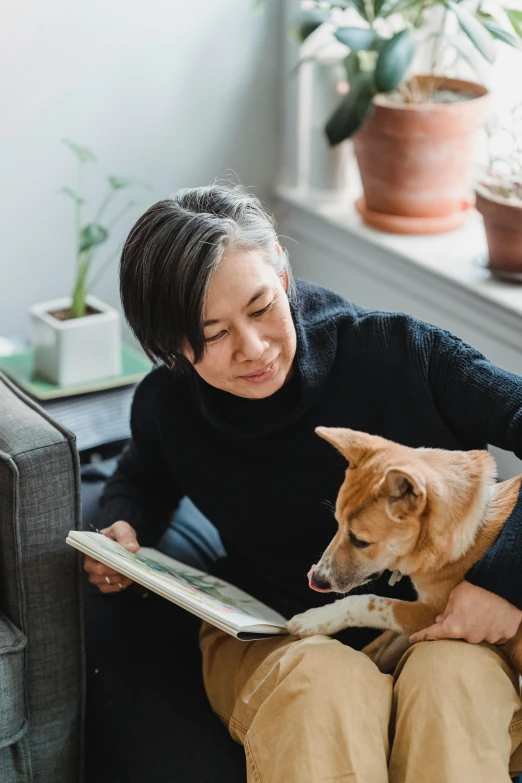 a woman sitting on a couch reading a book with a dog, asian descent, profile image, dwell, maintenance