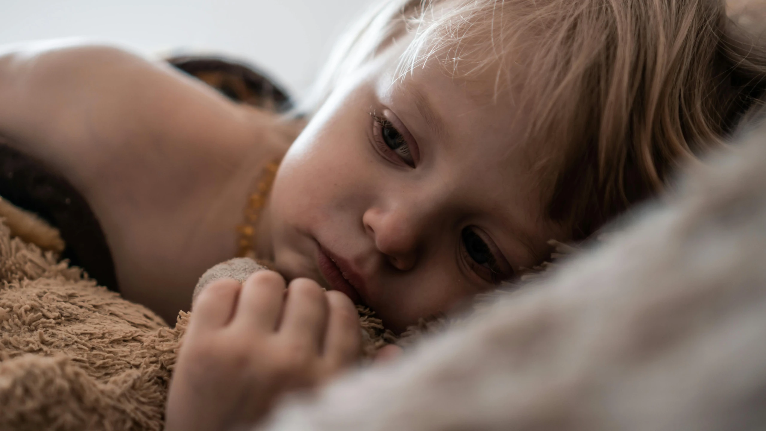 a little girl that is laying down with a teddy bear, by Ruth Simpson, trending on pexels, visual art, intricate heterochromia sad, curled up under the covers, close up at face, over his shoulder