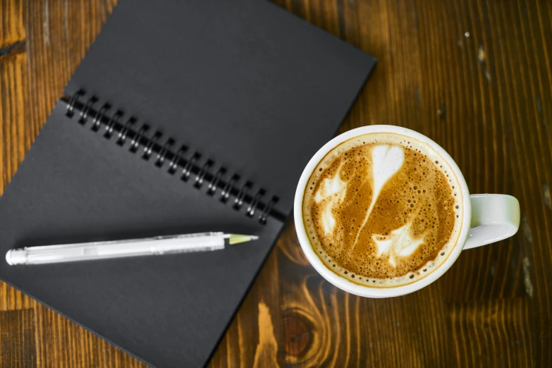 a cup of cappuccino next to a notebook on a wooden table, by Matt Cavotta, pexels contest winner, black, background image, no - text no - logo, group photo