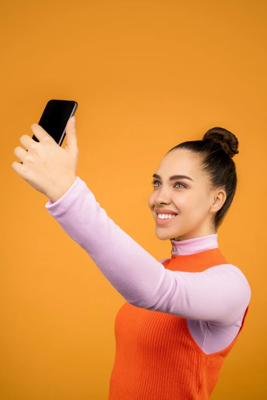 a woman taking a selfie with her cell phone, happening, orange color scheme, with a ponytail, solid background, gen z