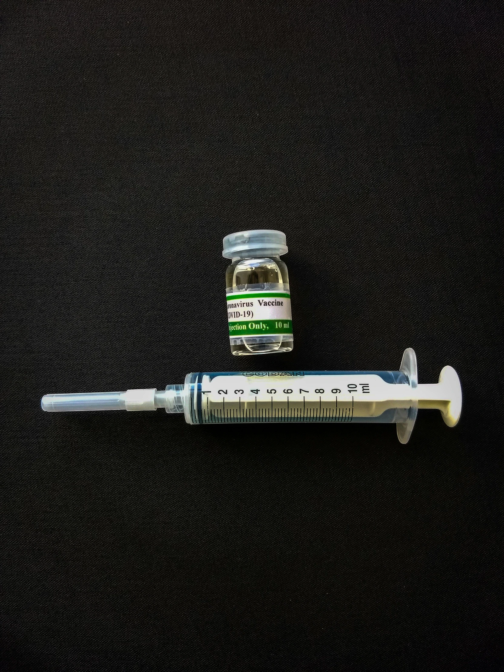 a syll sitting on top of a table next to a bottle of medicine, by Ben Zoeller, syringe, on a black background, embedded in clear epoxy, product image