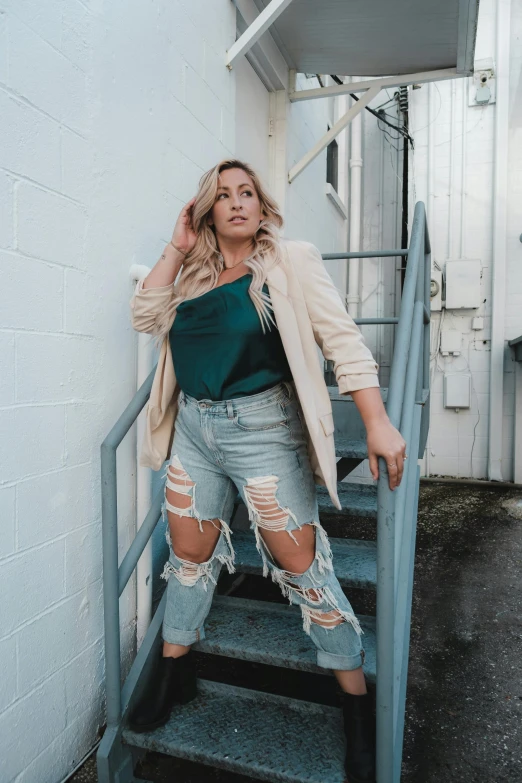 a woman in ripped jeans leaning against a wall, by Kristin Nelson, trending on pexels, renaissance, teal suit, alluring plus sized model, blonde woman, walking towards the camera