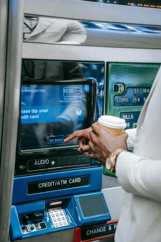 a man holding a cup of coffee in front of an atm machine, an album cover, by Matt Cavotta, pexels, nipsey hussle, technological screens, nyc, jamaica