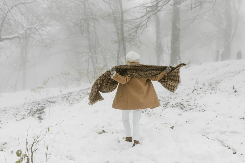 a woman in a coat is walking in the snow, by Lucia Peka, pexels contest winner, white scarf, browns and whites, be running up that hill, cottagecore