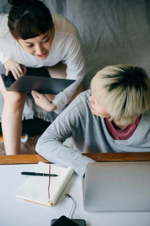 a couple of people sitting at a table with a laptop, by Jang Seung-eop, trending on pexels, top-down shot, teaching, woman holding another woman, no - text no - logo