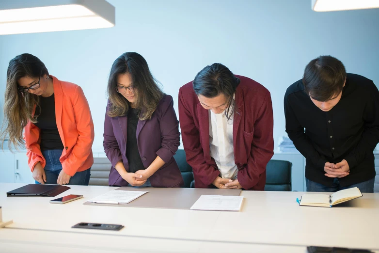 a group of people standing around a table, pexels contest winner, academic art, bent over posture, doing a prayer, mit technology review, writing a letter