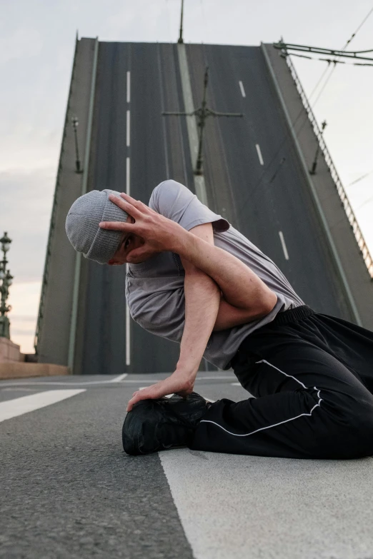 a man sitting on the ground in front of a bridge, dynamic stretching, in russia, head tilted down, 2019 trending photo