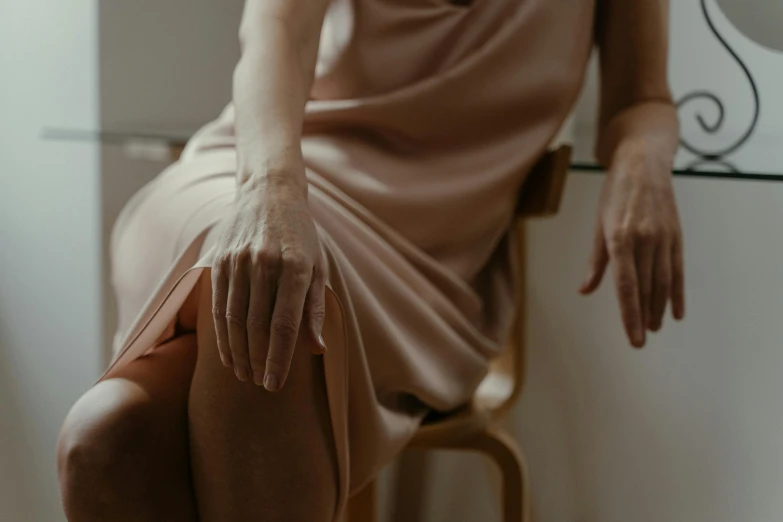 a woman sitting on top of a wooden chair, by Emma Andijewska, trending on pexels, aestheticism, close-up of thin soft hand, dressed in a pink dress, visible veins, sitting in a lounge