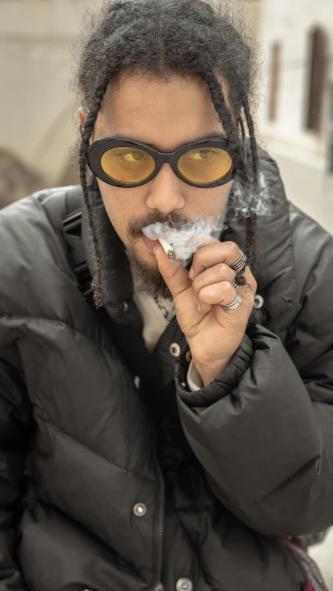 a man with dreadlocks smoking a cigarette, inspired by Jesse Richards, trending on unsplash, model wears a puffer jacket, with nerdy glasses and goatee, minn, inuit