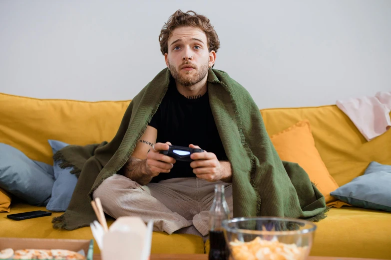 a man sitting on a couch holding a video game controller, by Adam Marczyński, pexels, renaissance, wearing a green cloak, annoyed, man wearing a closed cowl, avatar image