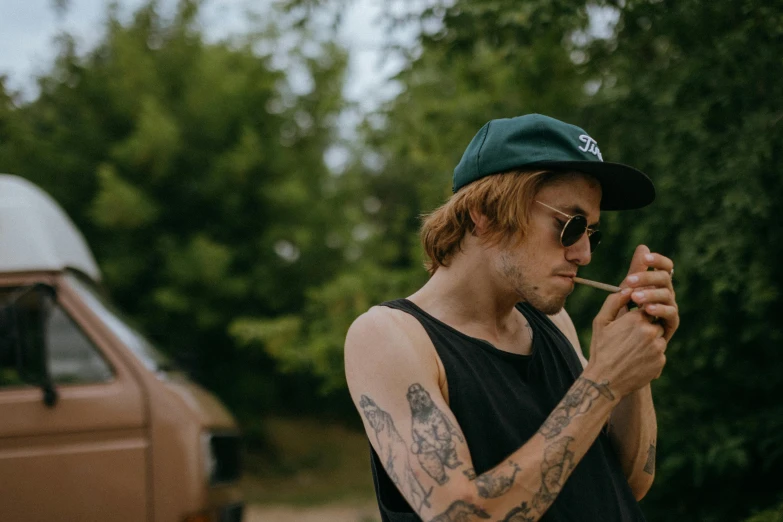 a man smoking a cigarette in front of a van, a tattoo, trending on pexels, joe keery, wearing sunglasses and a cap, thc, outdoors