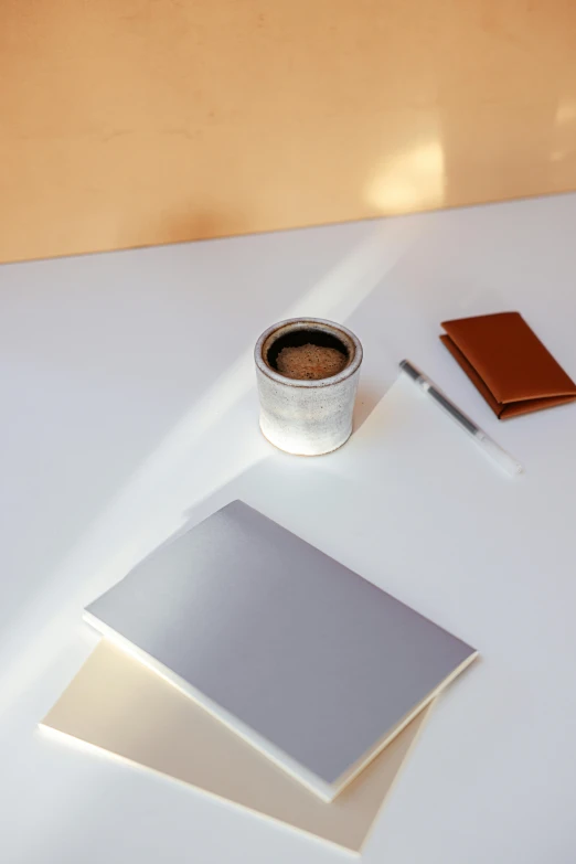 a cup of coffee sitting on top of a white table, by Carey Morris, light and space, gradient brown to silver, holding notebook, product view, desks