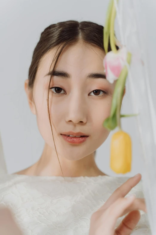 a woman holding a flower in front of her face, inspired by Zhang Yan, trending on pexels, hyperrealism, square facial structure, white hanfu, ethnicity : japanese, wearing organza gown